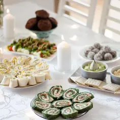 Stół z przekąskami na przyjęcie: roladki z tortilli, zielone rolmopsy, dipy, ciasteczka i babeczki.